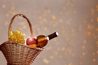 Photo of Bottles of wine in wicker basket with bow against blurred lights. Space for text