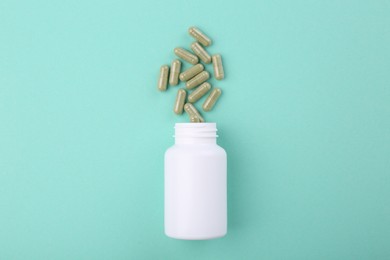 Photo of Bottle and vitamin capsules on turquoise background, top view