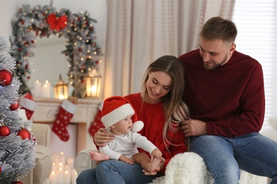 Photo of Happy family with cute baby in room decorated for Christmas holiday