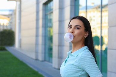 Beautiful woman blowing gum near building outdoors, space for text