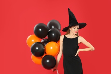 Photo of Beautiful woman wearing witch costume with balloons for Halloween party on red background