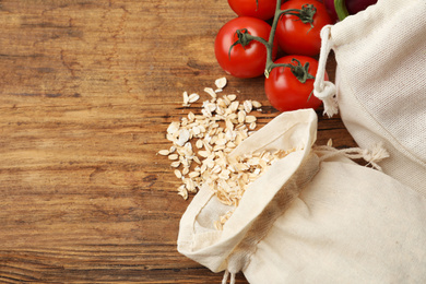 Cotton eco bags with vegetables and oat flakes on wooden table, flat lay. Space for text