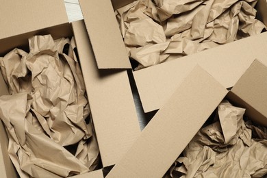 Open cardboard boxes with crumpled paper on white wooden floor, flat lay