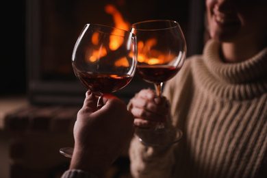 Photo of Couple with glasses of red wine near fireplace, closeup