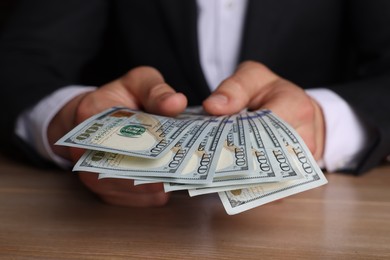 Money exchange. Man counting dollar banknotes at wooden table, closeup