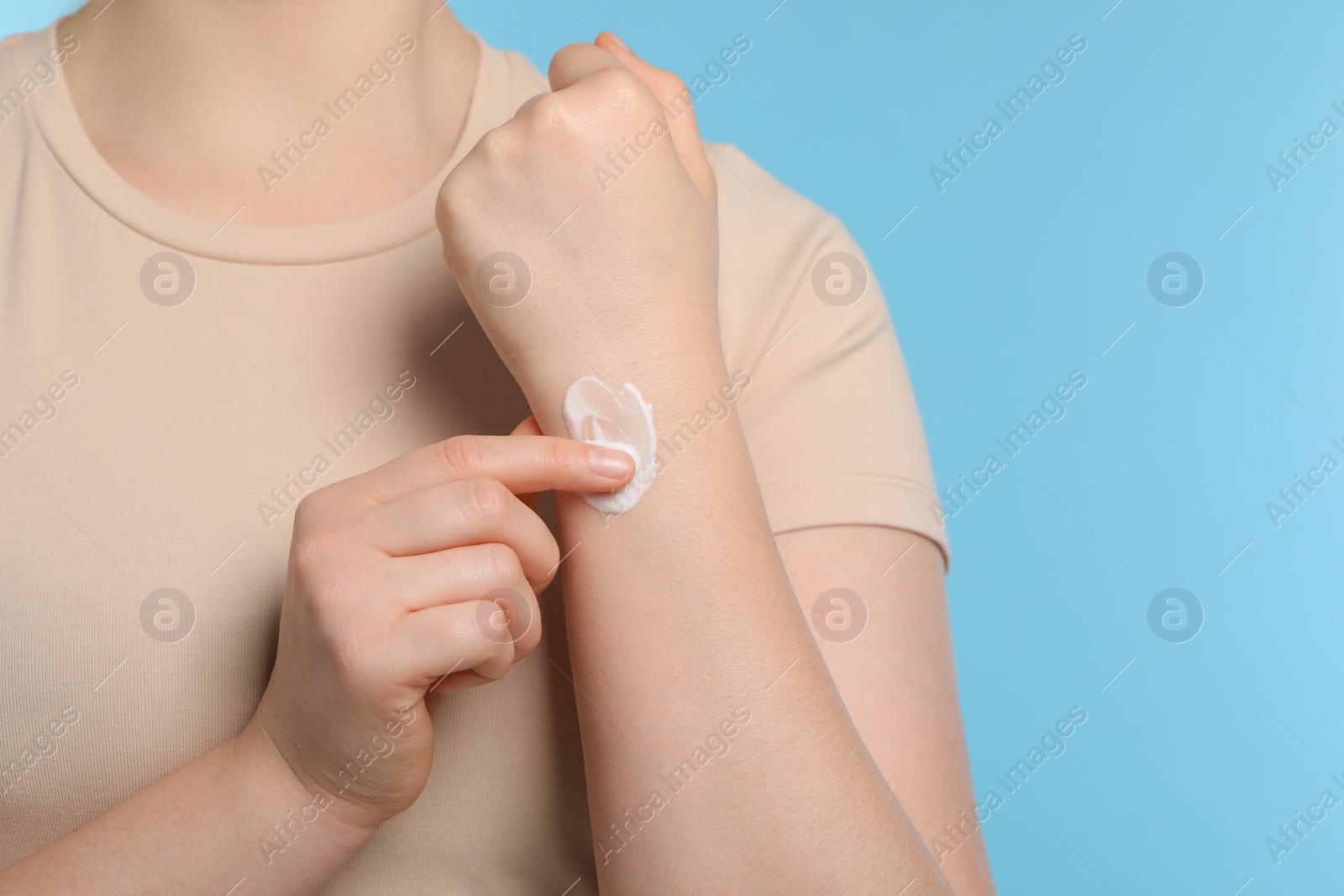 Photo of Woman applying ointment onto her hand on light blue background, closeup