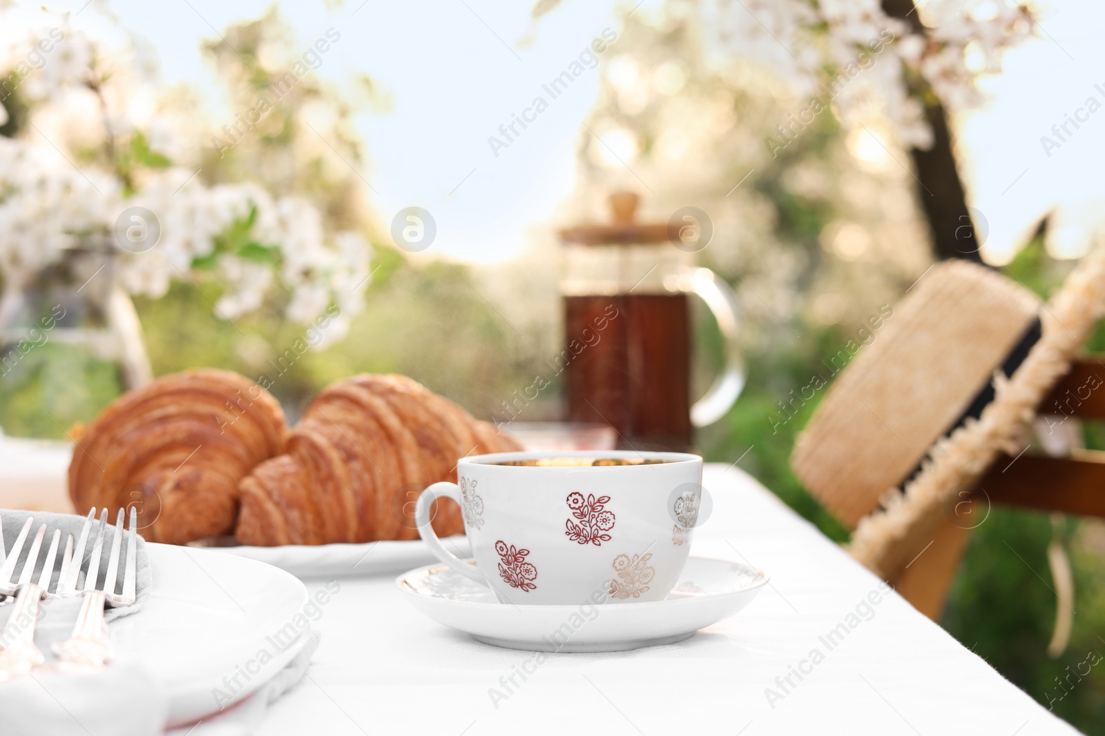 Photo of Stylish table setting with tea and croissants in spring garden