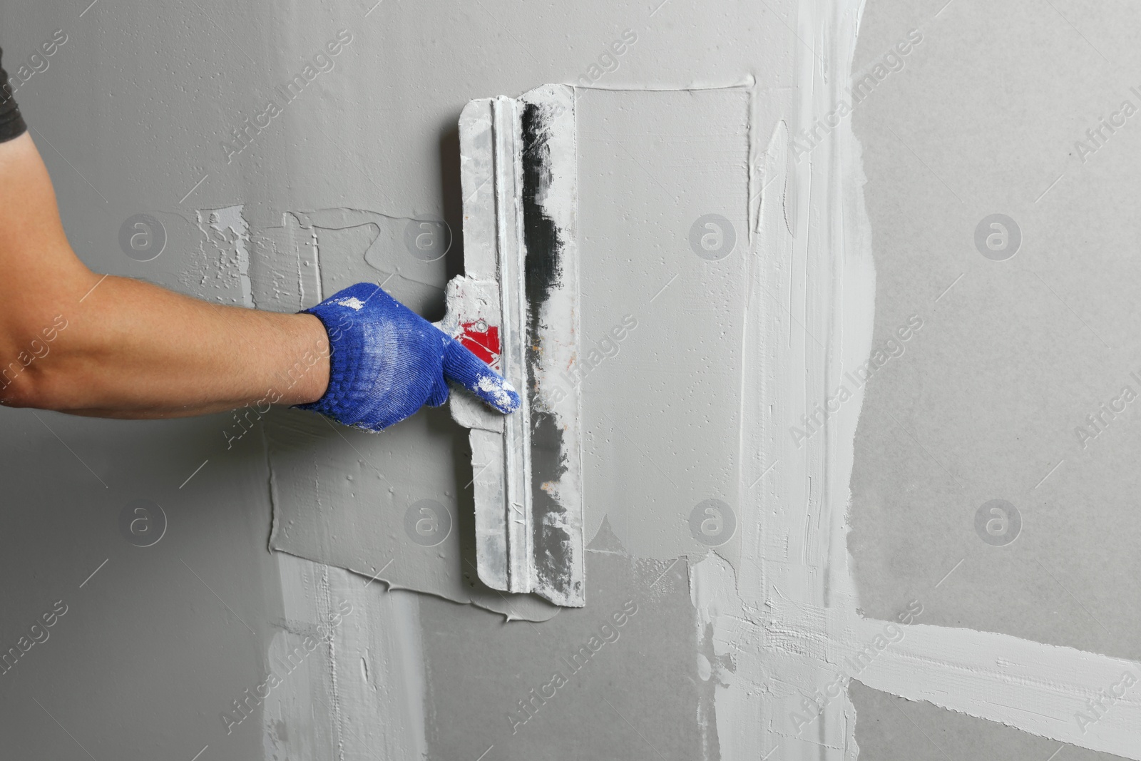 Photo of Professional worker plastering wall with putty knife, closeup