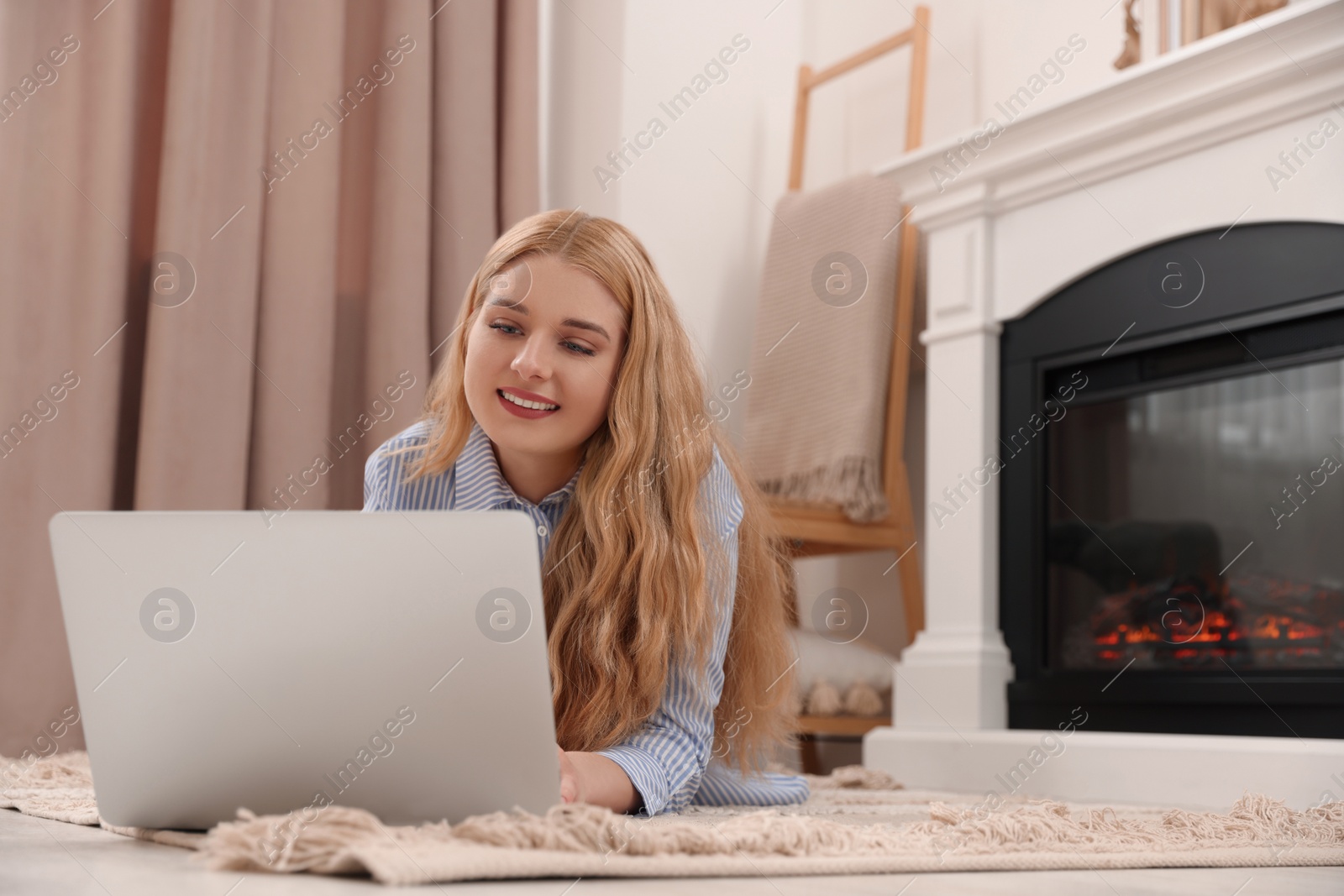 Photo of Young woman working on laptop near fireplace in room