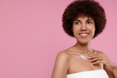 Beautiful young woman applying cream onto body on pink background, space for text