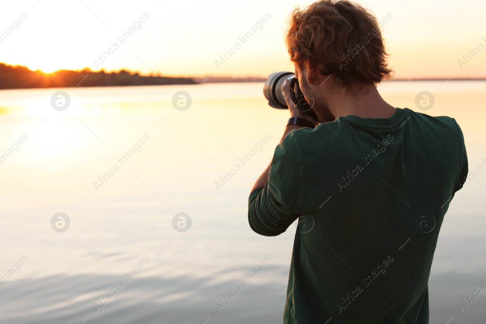 Photo of Male photographer taking photo of riverside sunset with professional camera outdoors