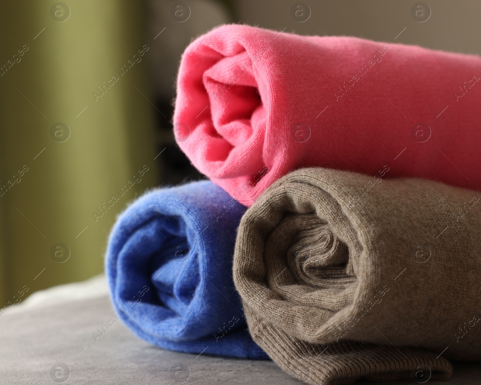 Photo of Rolled color sweaters on gray table, closeup. Space for text