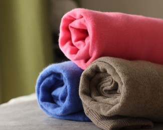 Rolled color sweaters on gray table, closeup. Space for text