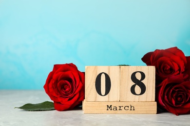 Wooden block calendar with date 8th of March and roses on table against light blue background, space for text. International Women's Day