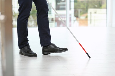 Photo of Blind person with long cane walking indoors, closeup
