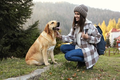 Happy woman and adorable dog sitting on green grass in mountains. Traveling with pet