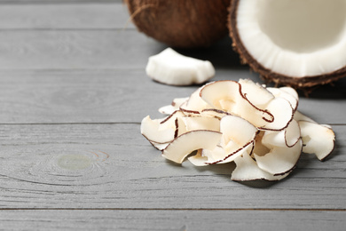 Photo of Pile of tasty coconut chips on grey wooden table. Space for text