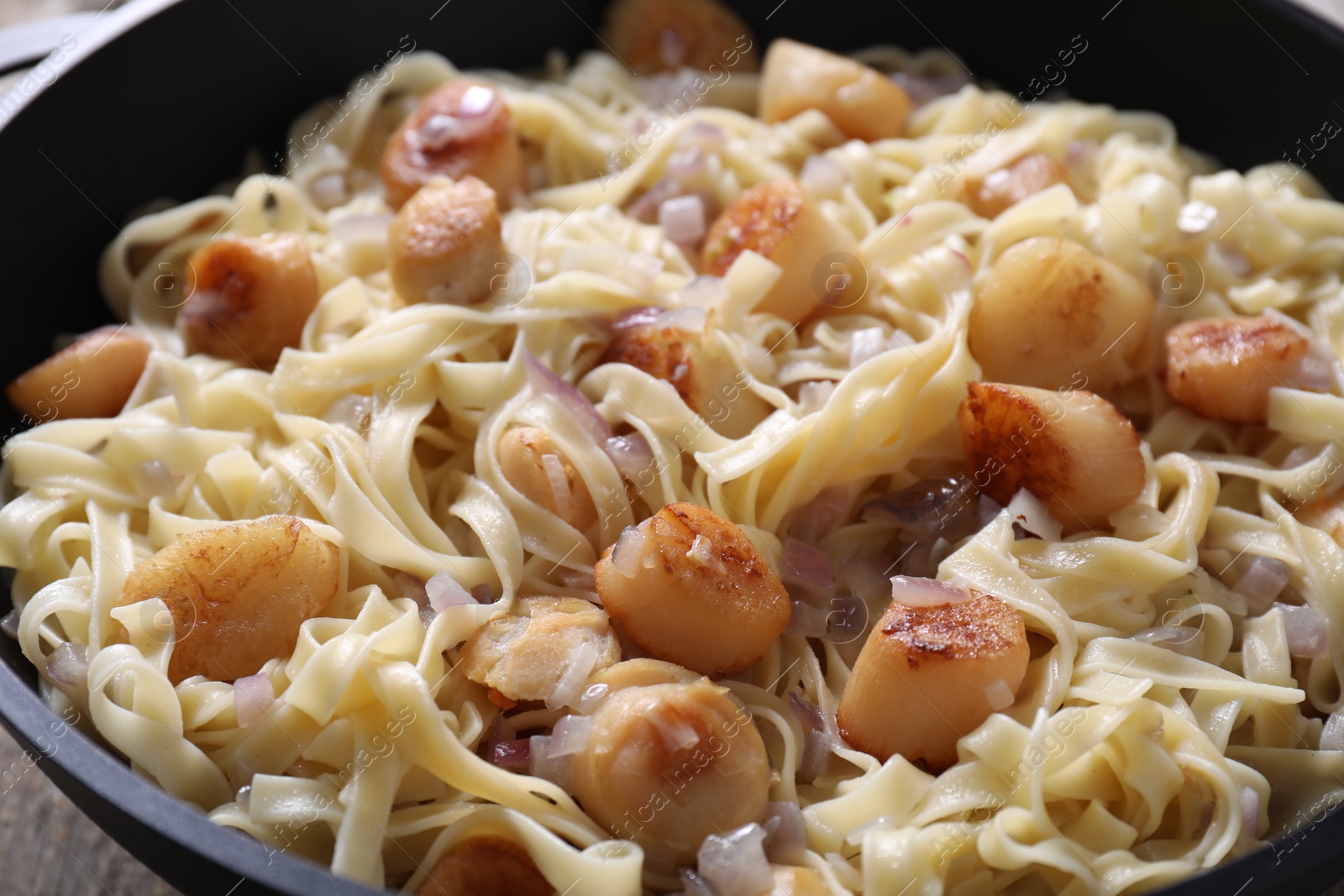 Photo of Delicious scallop pasta with onion in bowl, closeup