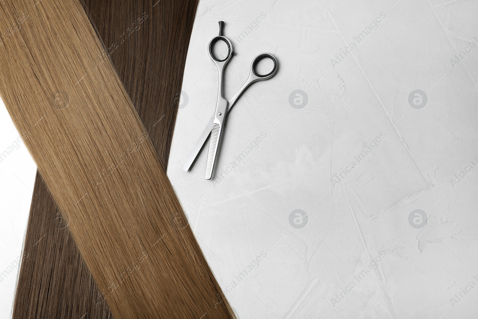 Photo of Straight brown hair and thinning scissors on light background, flat lay. Space for text