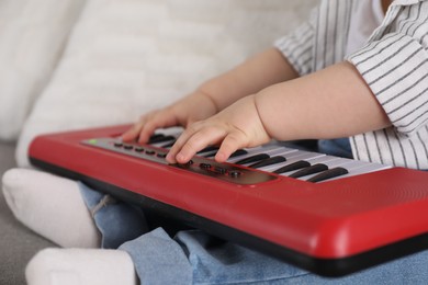 Photo of Little child playing toy piano indoors, closeup
