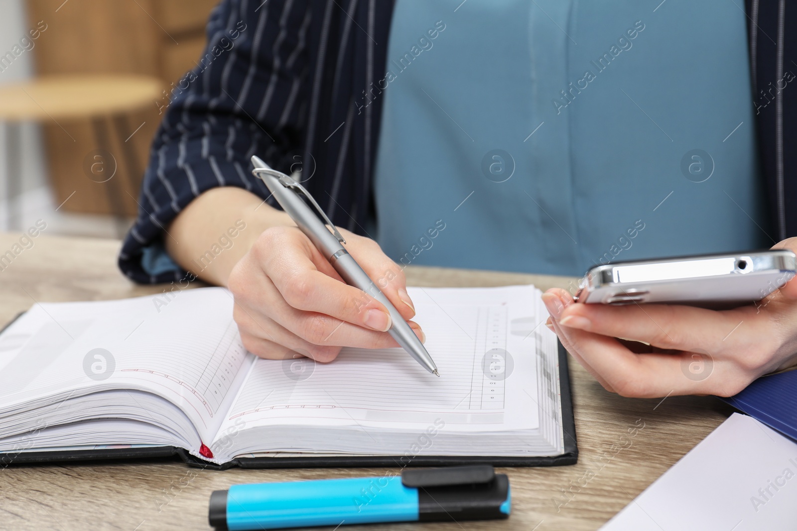 Photo of Woman taking notes while using smartphone at wooden table, closeup