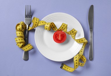 Photo of Plate with cut tomato, cutlery and measuring tape on light purple background, flat lay. Diet concept