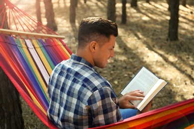 Man with book relaxing in hammock outdoors on summer day