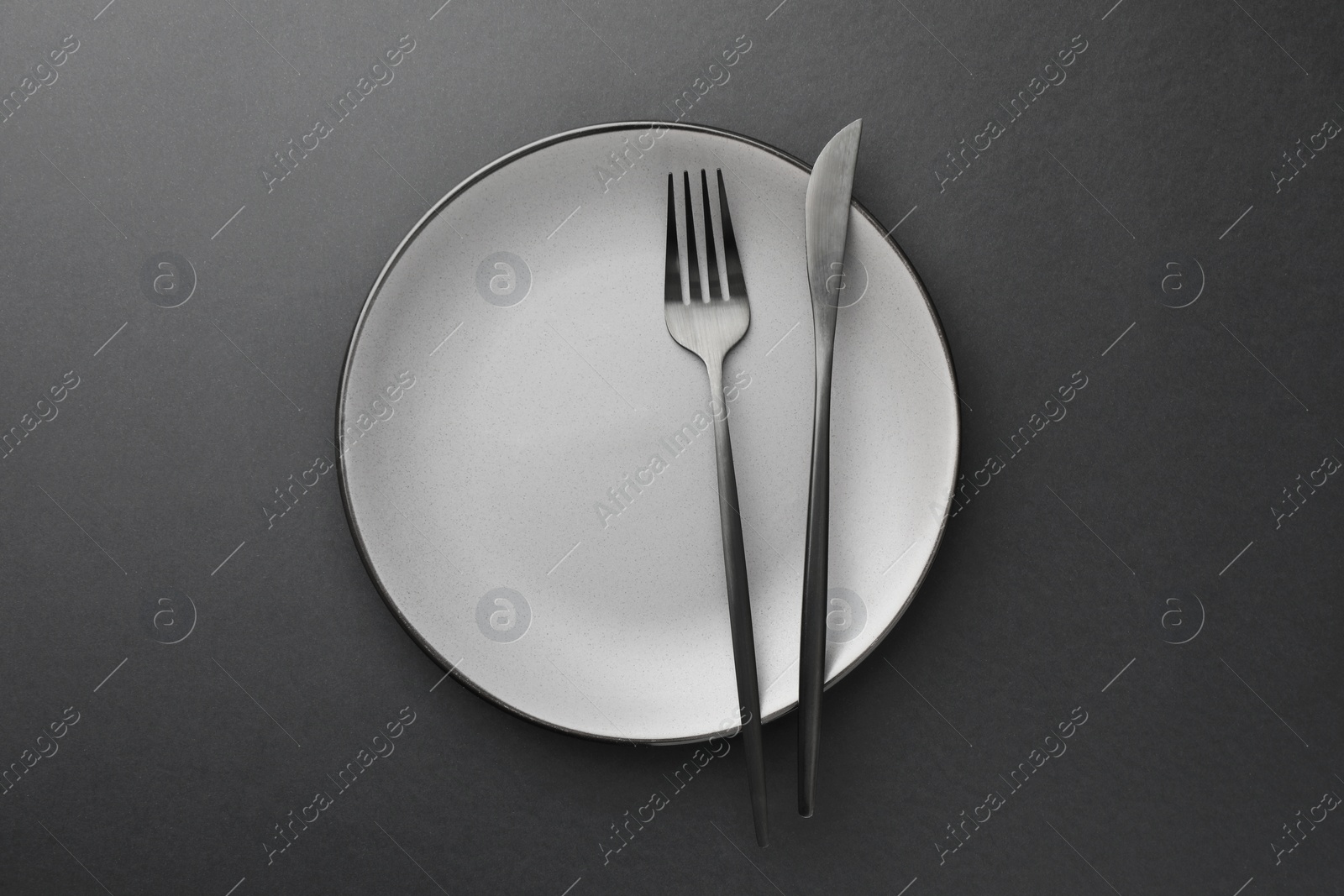 Photo of Clean plate, fork and knife on grey table, top view