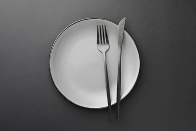 Clean plate, fork and knife on grey table, top view