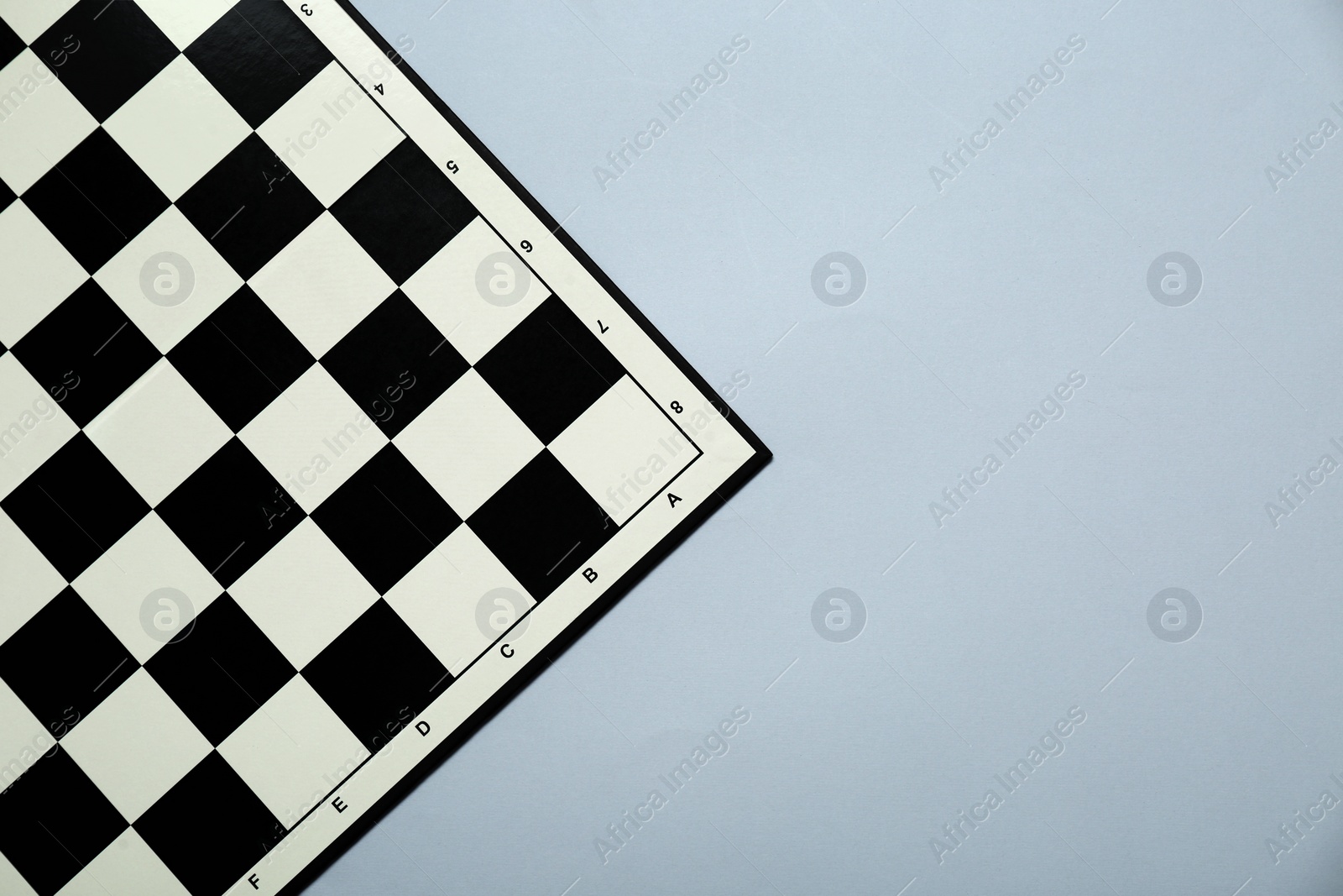 Photo of Black and white empty checkerboard on light grey background, top view. Space for text