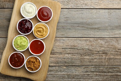 Different tasty sauces in bowls on wooden table, top view. Space for text