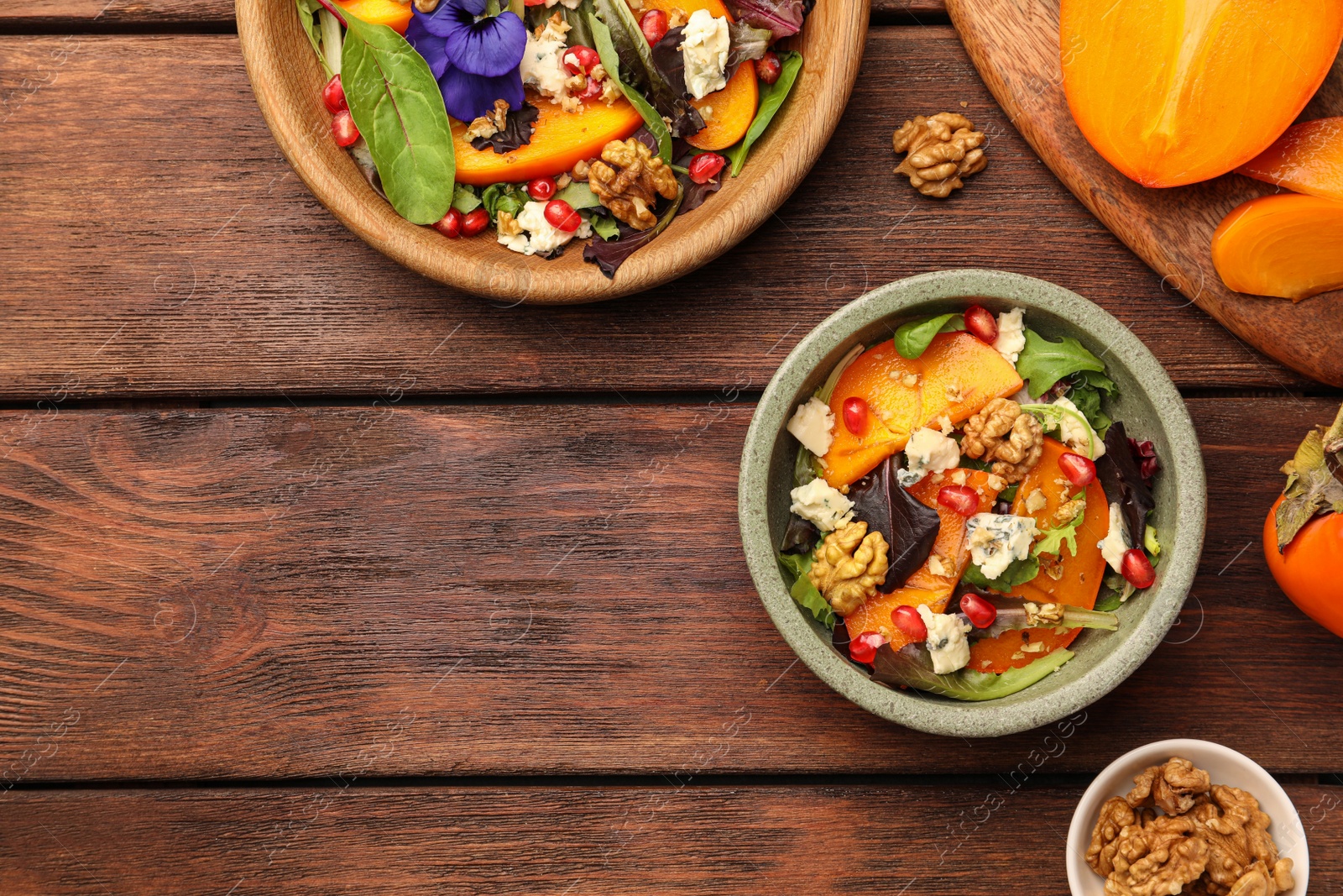 Photo of Delicious persimmon salad with cheese and pomegranate served on wooden table, flat lay. Space for text