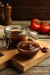 Photo of Tasty barbeque sauce in bowl, jar and spoon on wooden table