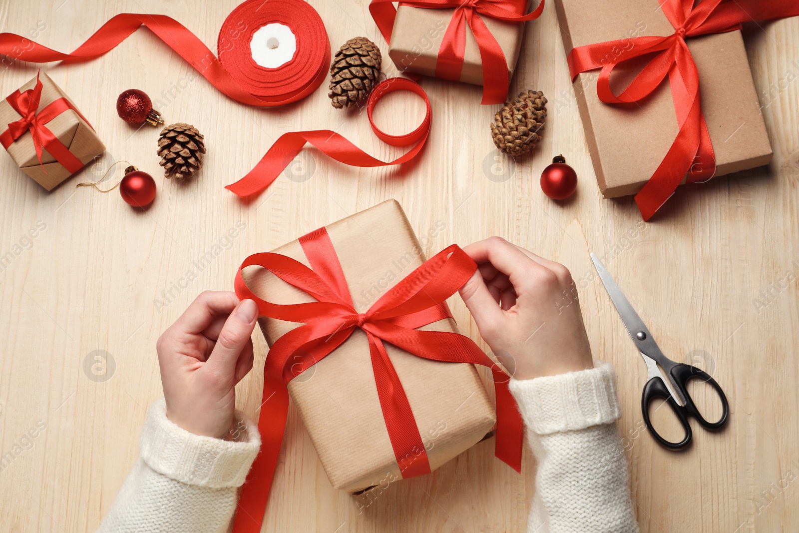 Photo of Christmas present. Woman tying ribbon bow on gift box at wooden table, top view