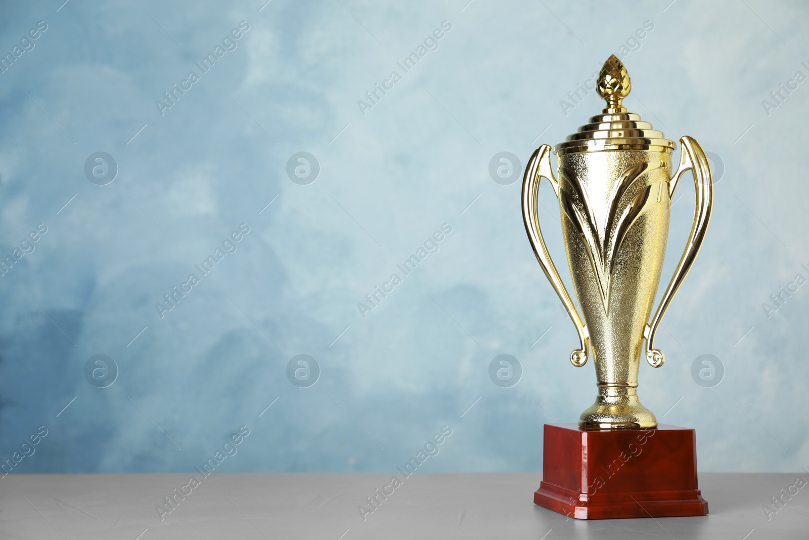 Photo of Golden trophy cup on table against blue background. Space for text