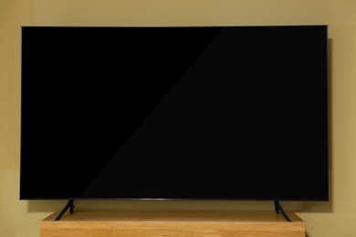 Modern plasma TV on wooden table near beige wall