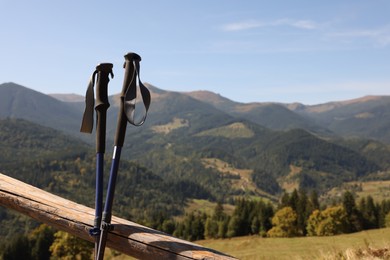 Trekking poles near wooden railing and picturesque view of mountain landscape as background. Space for text