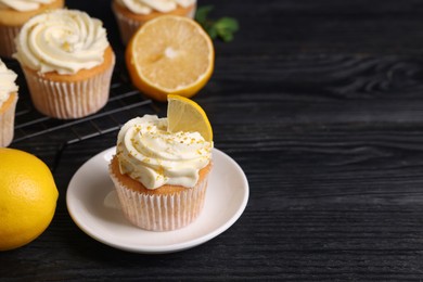 Photo of Delicious cupcakes with white cream, lemon zest and lemons on black wooden table, closeup. Space for text