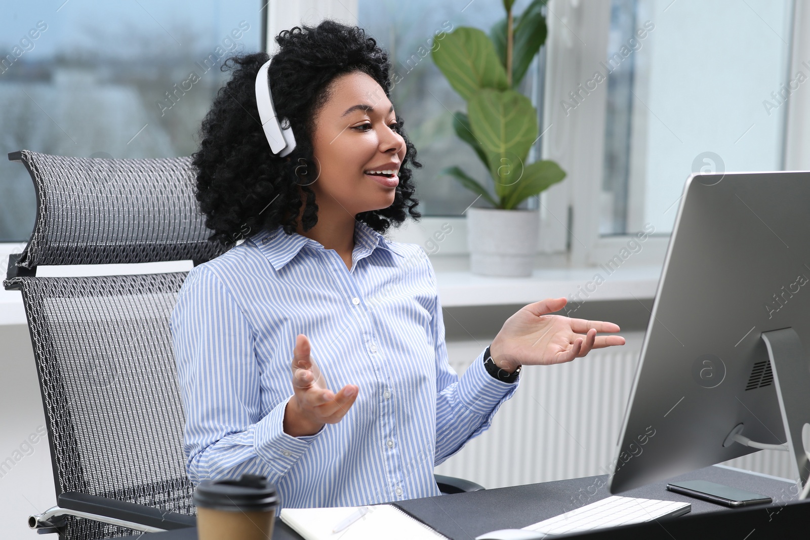 Photo of Young woman with headphones having video chat via computer in office