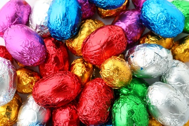 Photo of Many chocolate eggs wrapped in bright foil as background, top view