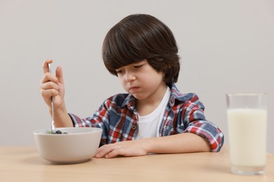 Cute little boy refusing to eat his breakfast at table on grey background
