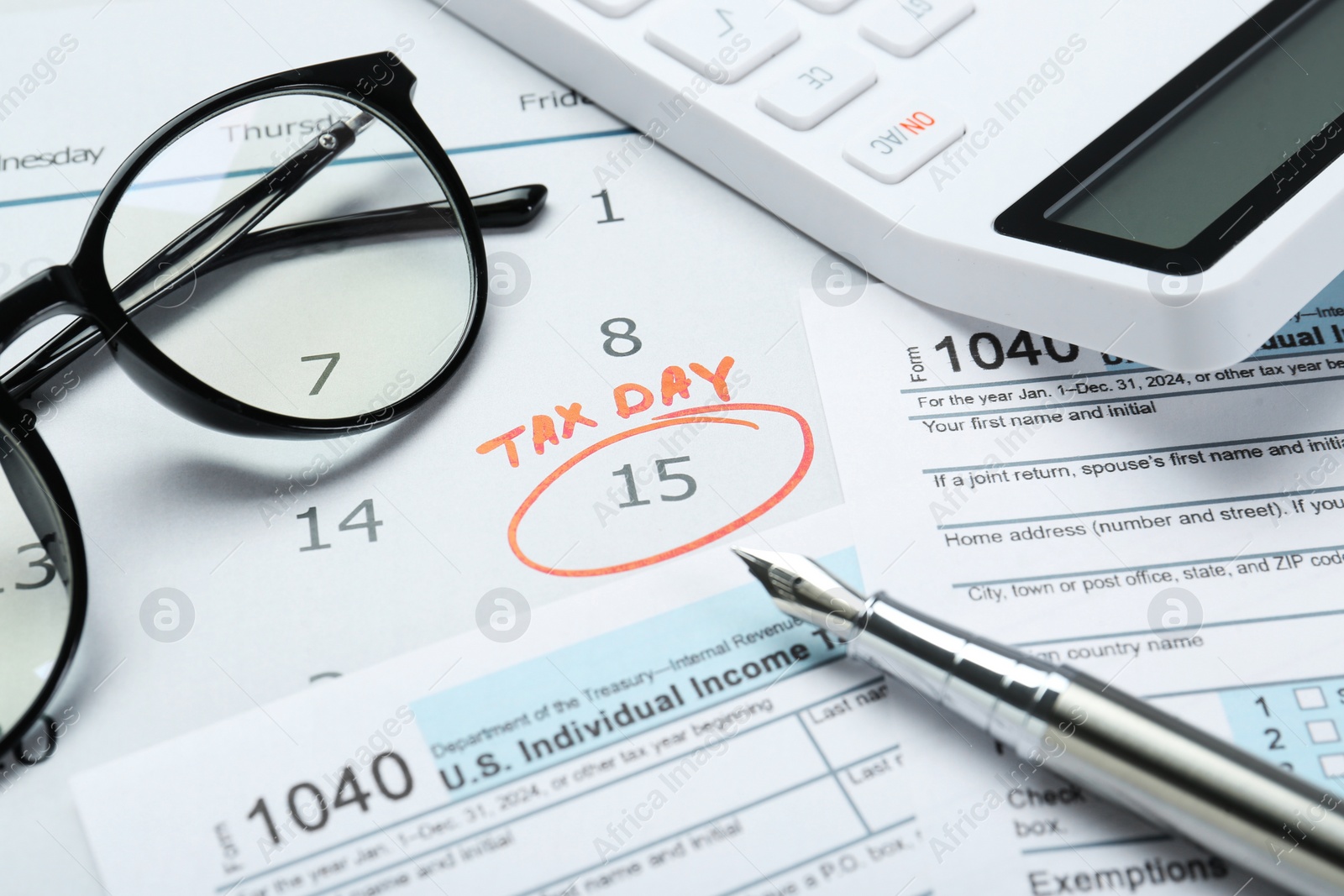 Photo of Tax day. Calendar with date reminder, documents, pen, calculator and glasses on table