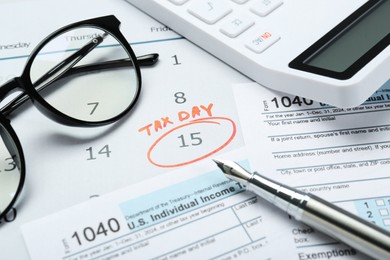 Photo of Tax day. Calendar with date reminder, documents, pen, calculator and glasses on table