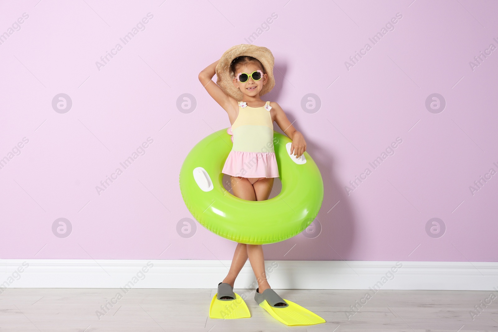 Photo of Cute little girl with inflatable ring wearing flippers near color wall