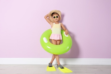 Cute little girl with inflatable ring wearing flippers near color wall