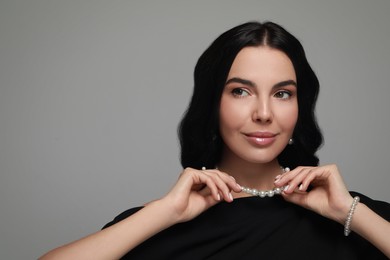 Photo of Young woman wearing elegant pearl jewelry on grey background, space for text