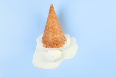 Photo of Melting ice cream and wafer cone on light blue background, top view