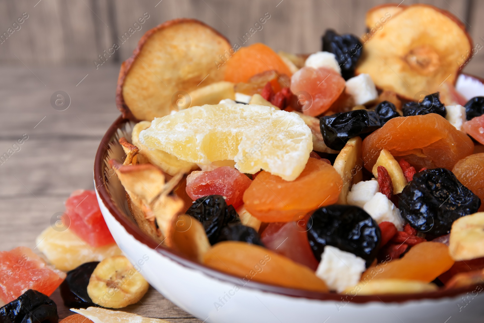 Photo of Bowl with different tasty dried fruits on wooden table, closeup