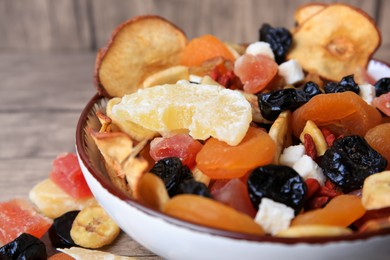Bowl with different tasty dried fruits on wooden table, closeup