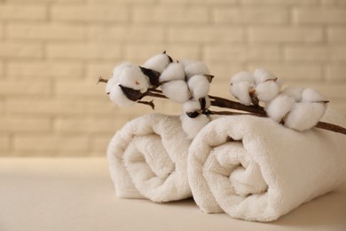 Photo of Rolled terry towels and cotton branch on white table near brick wall indoors, space for text